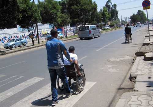 Addis Abeban kadulla toinen ihminen työntää toista pyörätuolissa