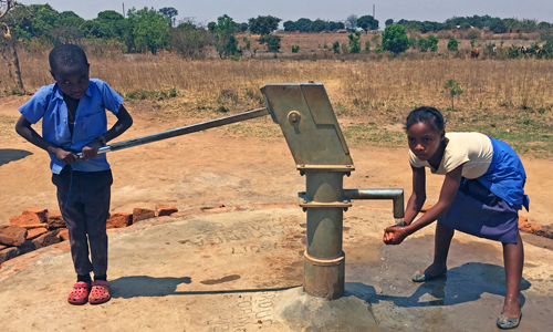Invalidiliiton lahjoittamalla kaivolla Sambian Kamuyngassa poika pumppaa vettä ja tyttö pesee käsiään.