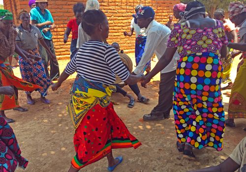 Sambialaisia tanssimassa piirissä, naisilla värikkäät hameet.