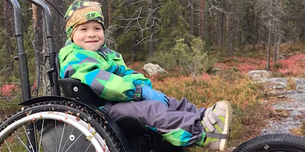 Hymyilevä Sisu-poika metsässä pyörätuolissa