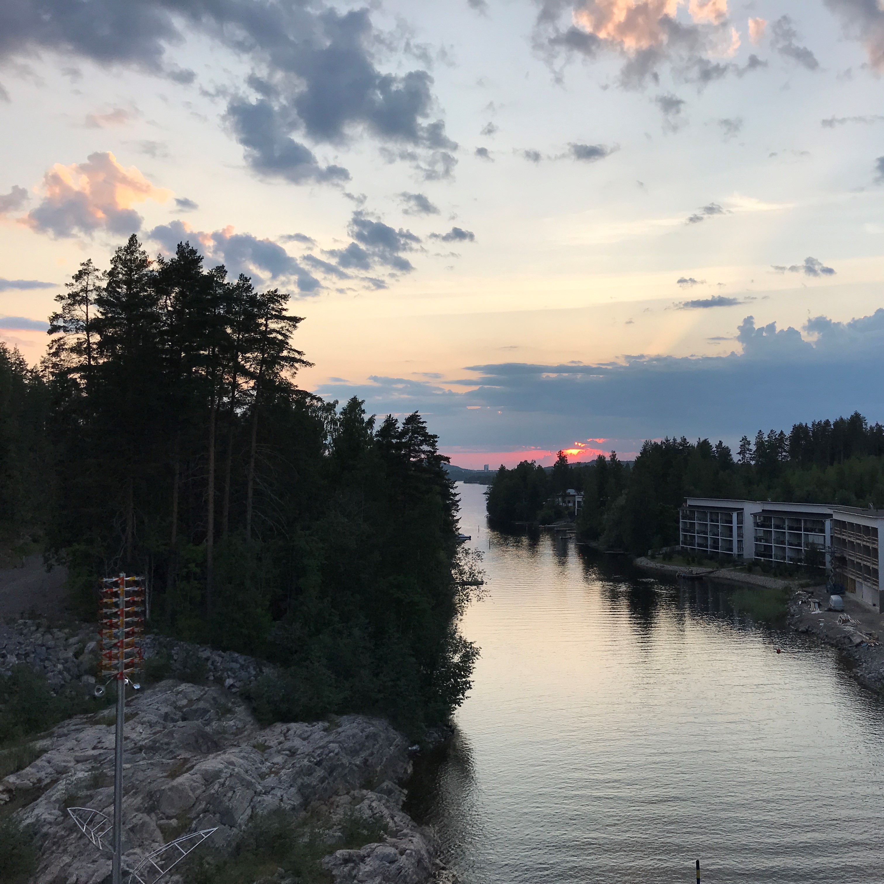 Kuvassa maisema auringonlaskun aikaan, jossa järvi, puita ja kiviä.