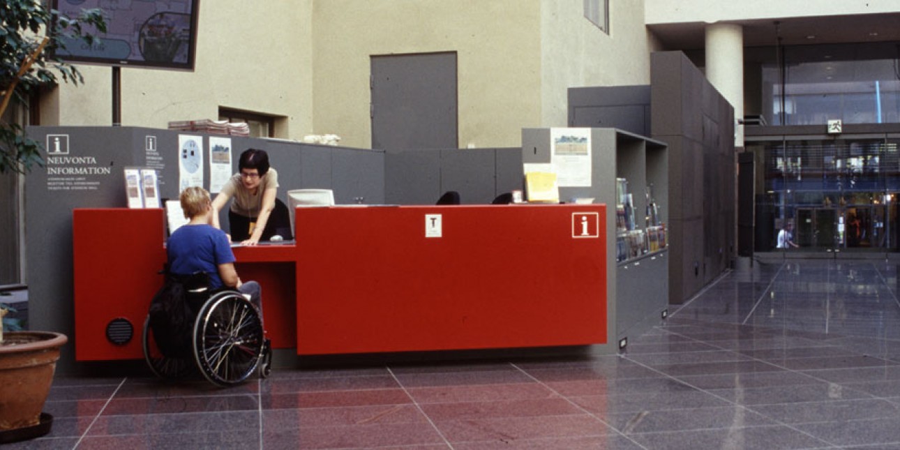 Valokuva matalasta palvelutiskistä ja pyörätuolissa istuva henkilö sen ääressä.
