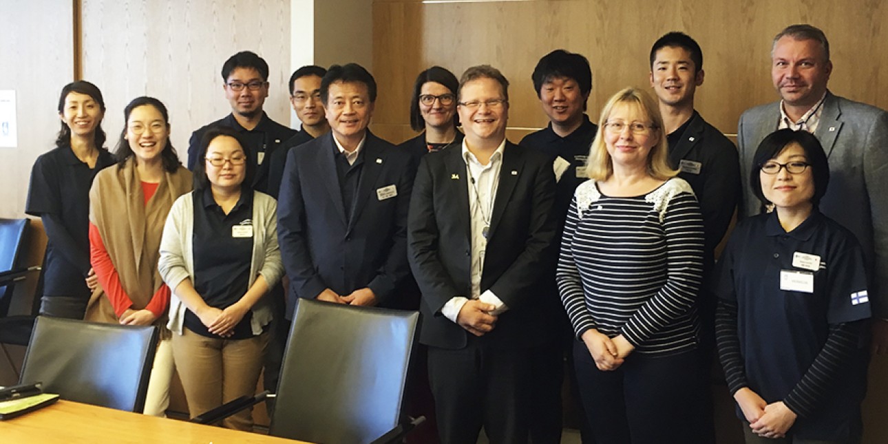 Kuvassa seisoo japanilaisia vieraita sekä invalidiliiton edustajia kokoustilassa.
