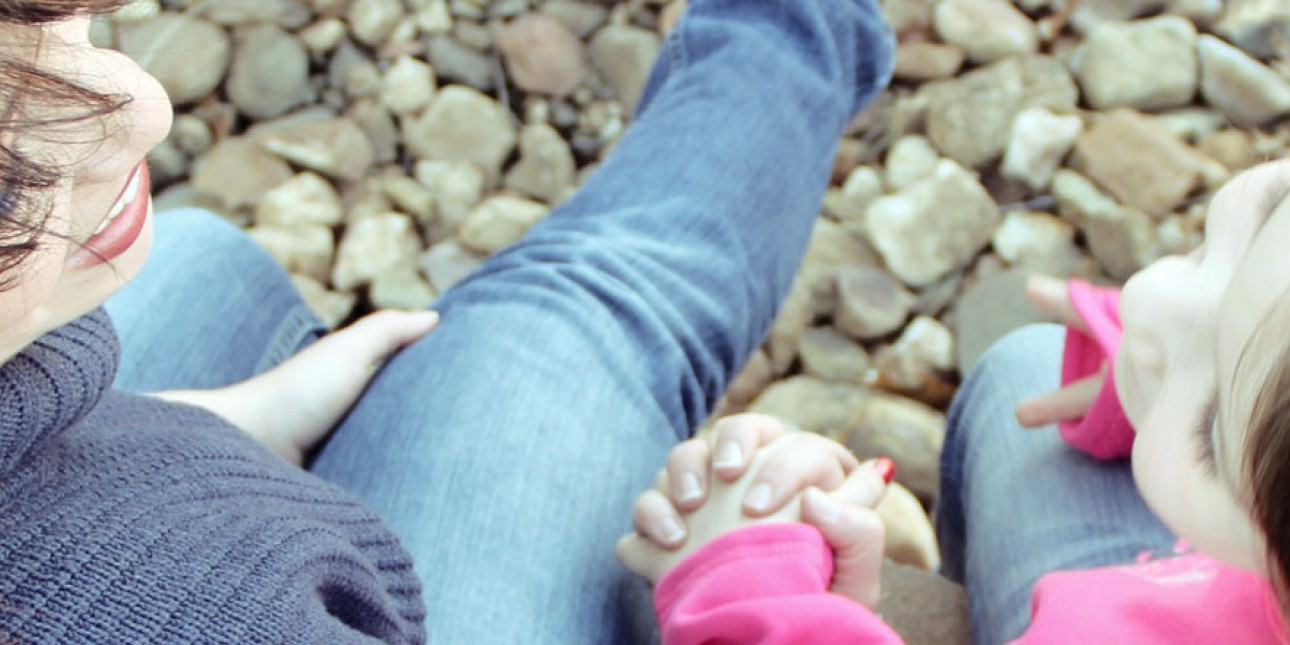 kuva äidistä ja tyttärestä käsi kädessä kivisellä rannalla