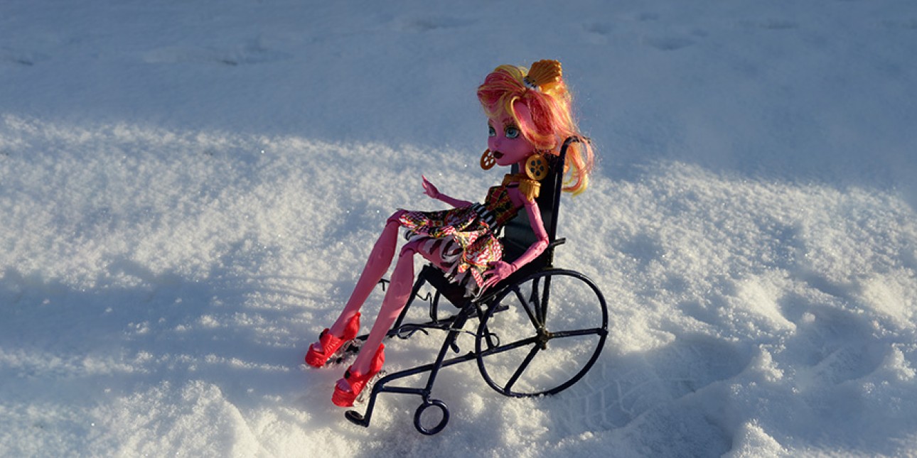 Barbie-nukke istuu pyörätuolissa ulkona.
