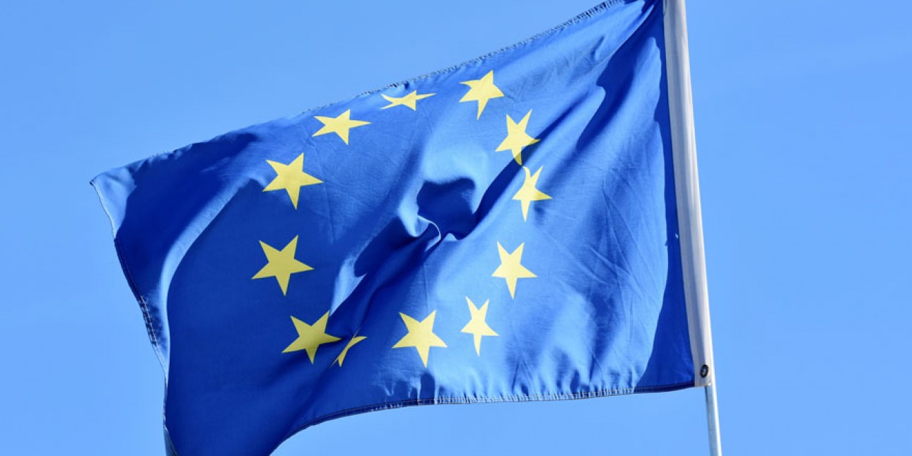 Sininen EU-lippu jossa keltaisia tähtiä ympyrässä liehumassa sinisellä taivaalla.