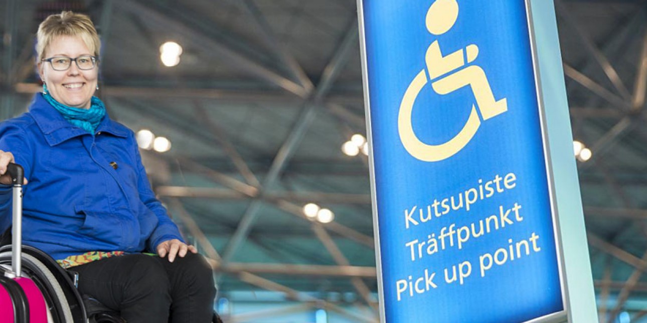 Pyörätuolissa istuva lentomatkustaja odottaa kutsupisteellä matkalaukun kanssa