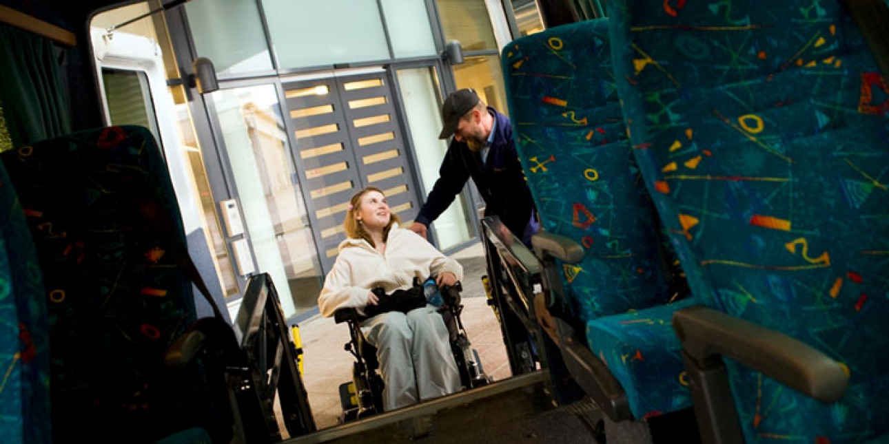 Inva-taksin kuljettaja auttaa pyörätuolissa istuvaa naisten sisään taksiin.
