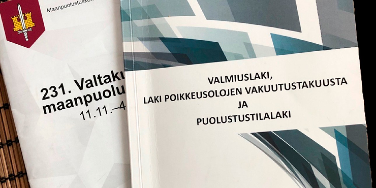 Valmiuslaki, Laki poikkeusolojen vakuutustakuusta ja puolustusilalaki-kirja ja sen takana osa Maanpuolustuskorkeakoulun kirjasta. Kuvituskuva.