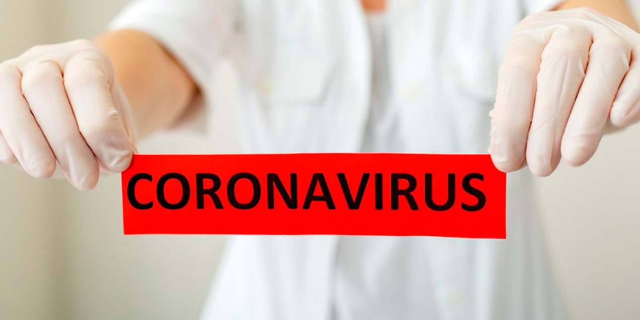 Suojakäsineet kädessä oleva ihminen pitää käsissään punaista lappua jossa lukee Coronavirus.