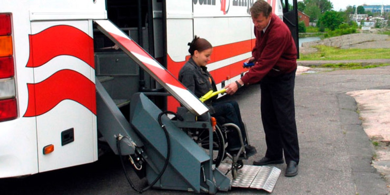 Kuljettaja auttaa pyörätuolissa istuvaa naista linja-autosta pois. Kuvituskuva.