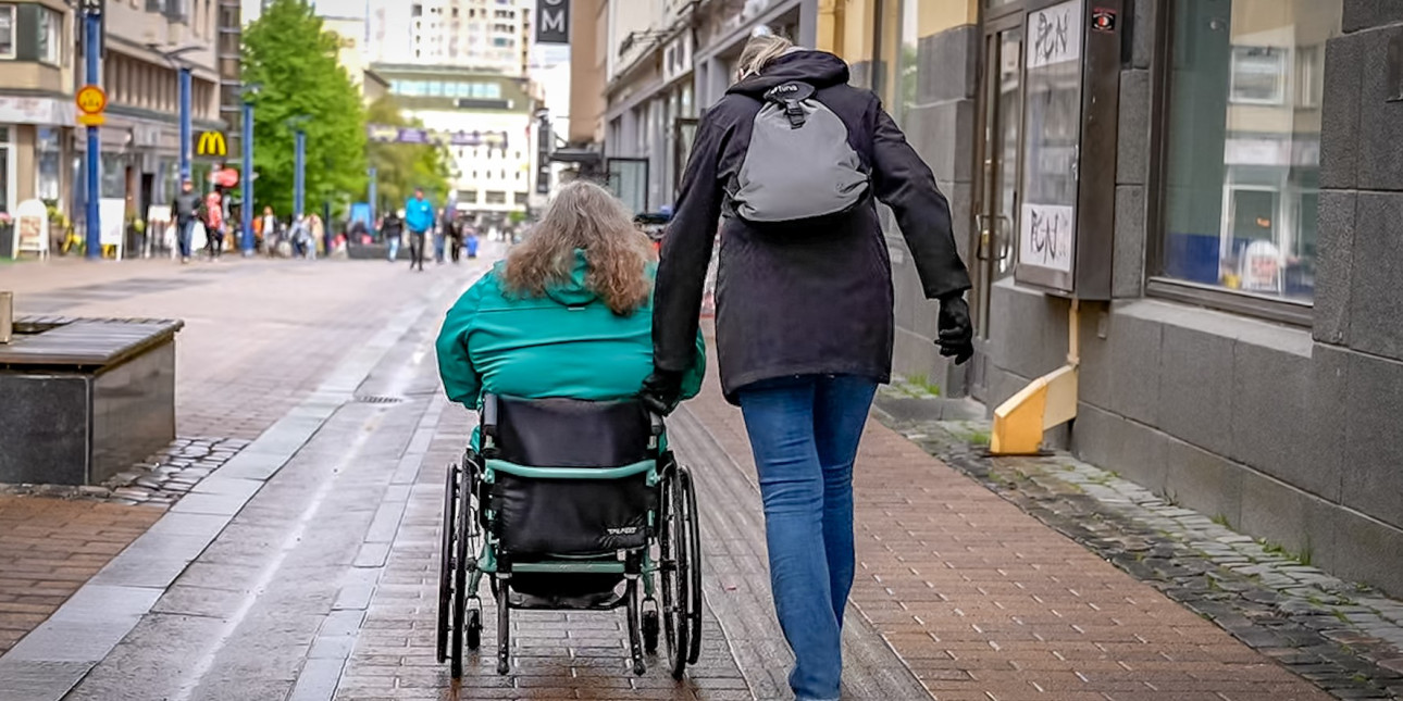 Pyörätuolilla liikkuva henkilö avustajansa kanssa kävelykadulla