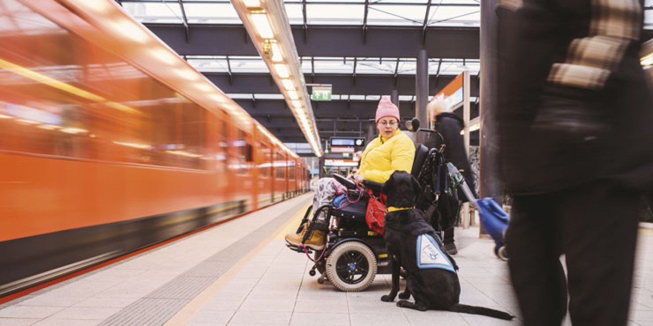 Pyörätuolilla liikkuva henkilö avustajakoiran kanssa metrolaiturilla
