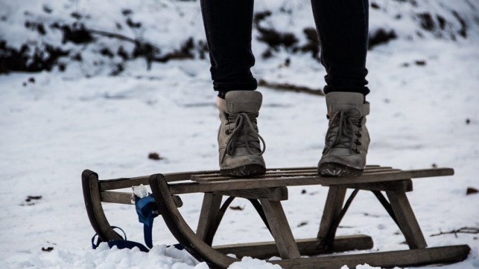 Puisen reen päällä seisomassa ihminen josta näkyy kuluneet nauhalliset talvikengät ja mustia housuja. Maa lumessa.