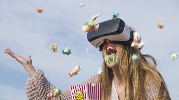 Kuvassa iloinen nainen VR lasit päässä heittelee popcorneja