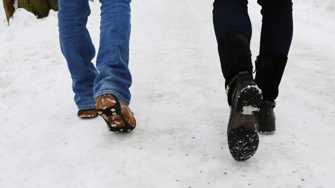 Lumisella tiellä kulkemassa kaksi ihmistä, Näkyvissä vain housunlahkeet ja kengänpohjat. Toisella on kengässä liukuesteet ja toisella nastat.