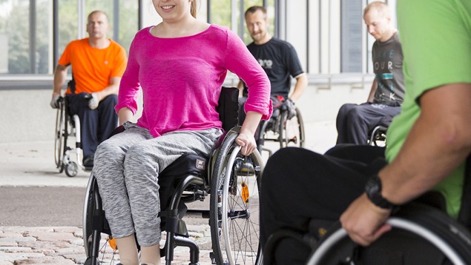 Pinkkipaitainen tyttö harjoittelee pyörätuolin käyttöä.