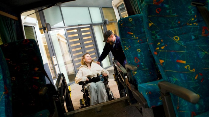 Inva-taksin kuljettaja auttaa pyörätuolissa istuvaa naisten sisään taksiin.
