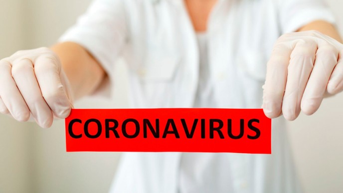 Suojakäsineet kädessä oleva ihminen pitää käsissään punaista lappua jossa lukee Coronavirus.