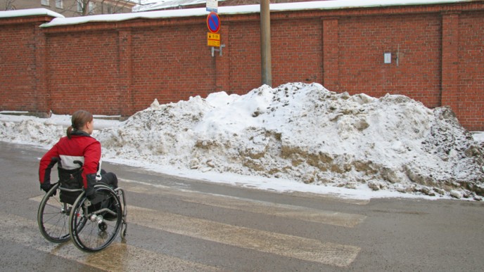 Ihminen pyörätuolissa suojatiellä jonka edesssä lumikasa.
