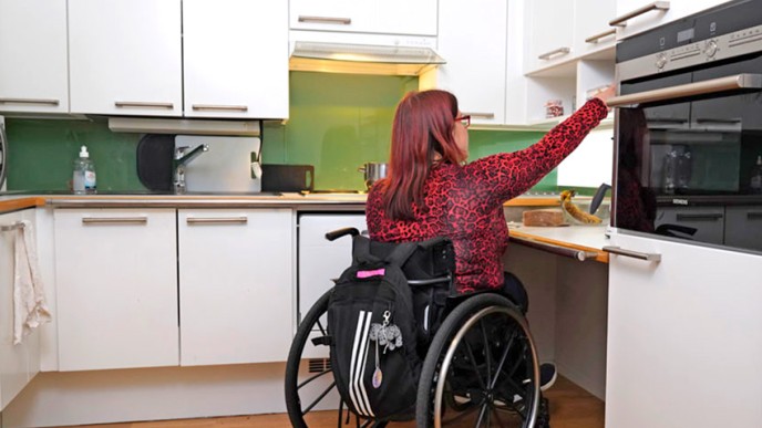 Pyörätuolia käyttävä nainen kurkottaa keittiön kaappiin. 