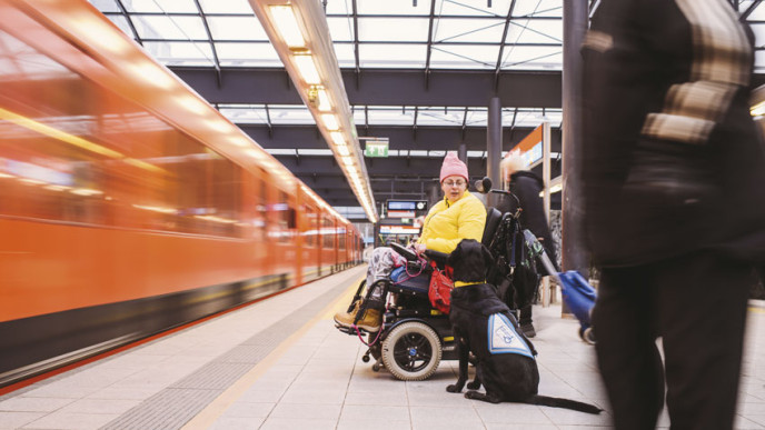 Pyörätuolilla liikkuva henkilö avustajakoiran kanssa metrolaiturilla